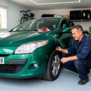 Hombre realizando una revisión pre-ITV casera a un coche Renault Megane verde en el garaje de su casa